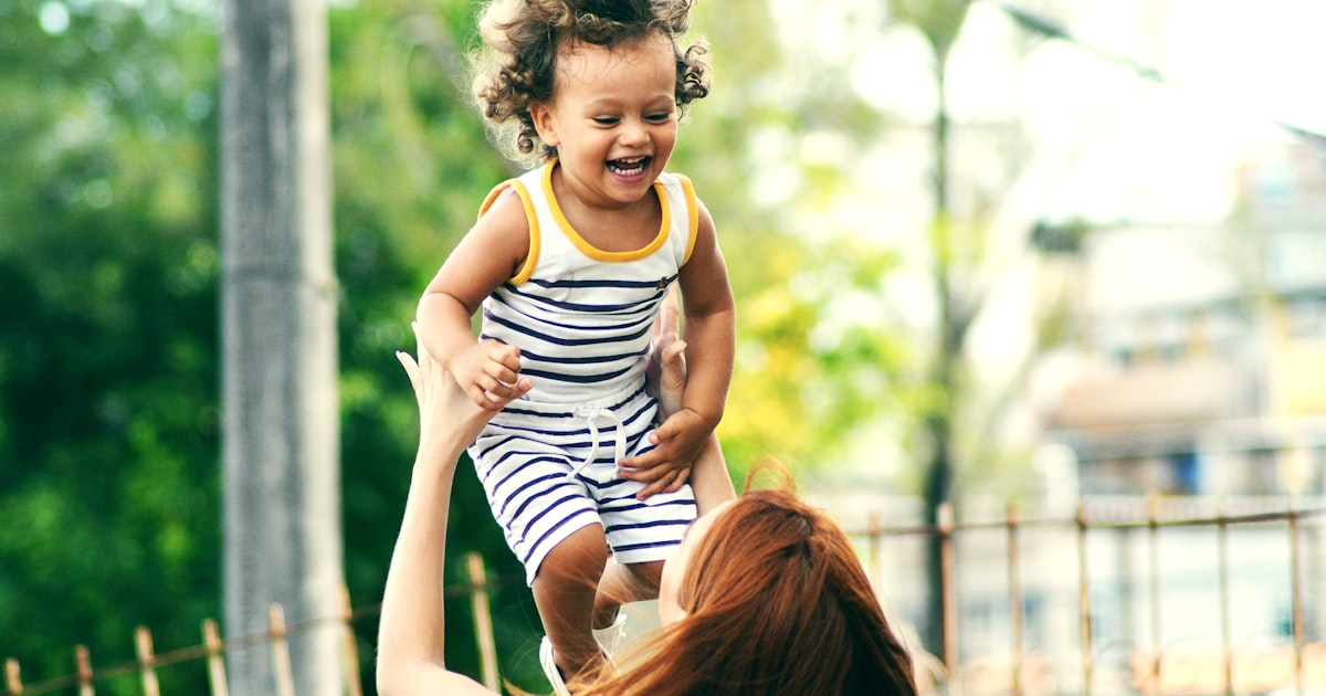 Caring adult lifting and supporting a young child outdoors in natural light