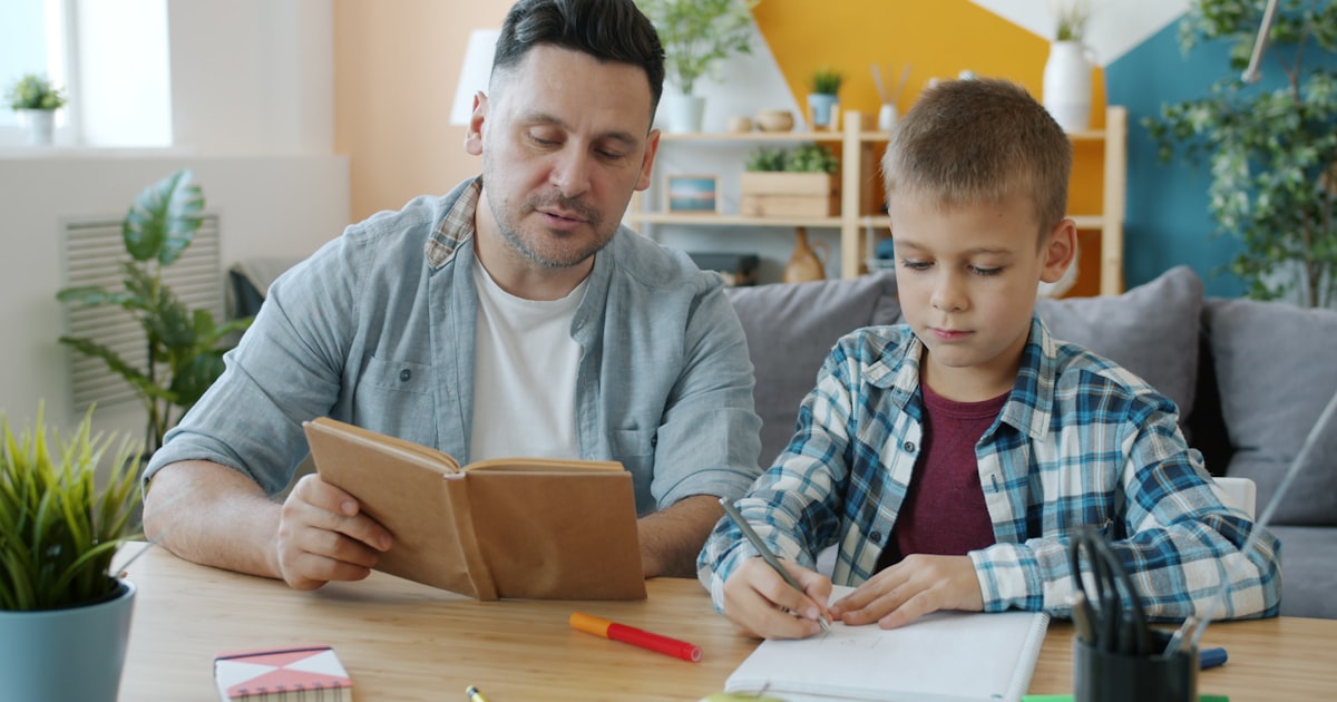 Father and child learning together, reading and writing at a table